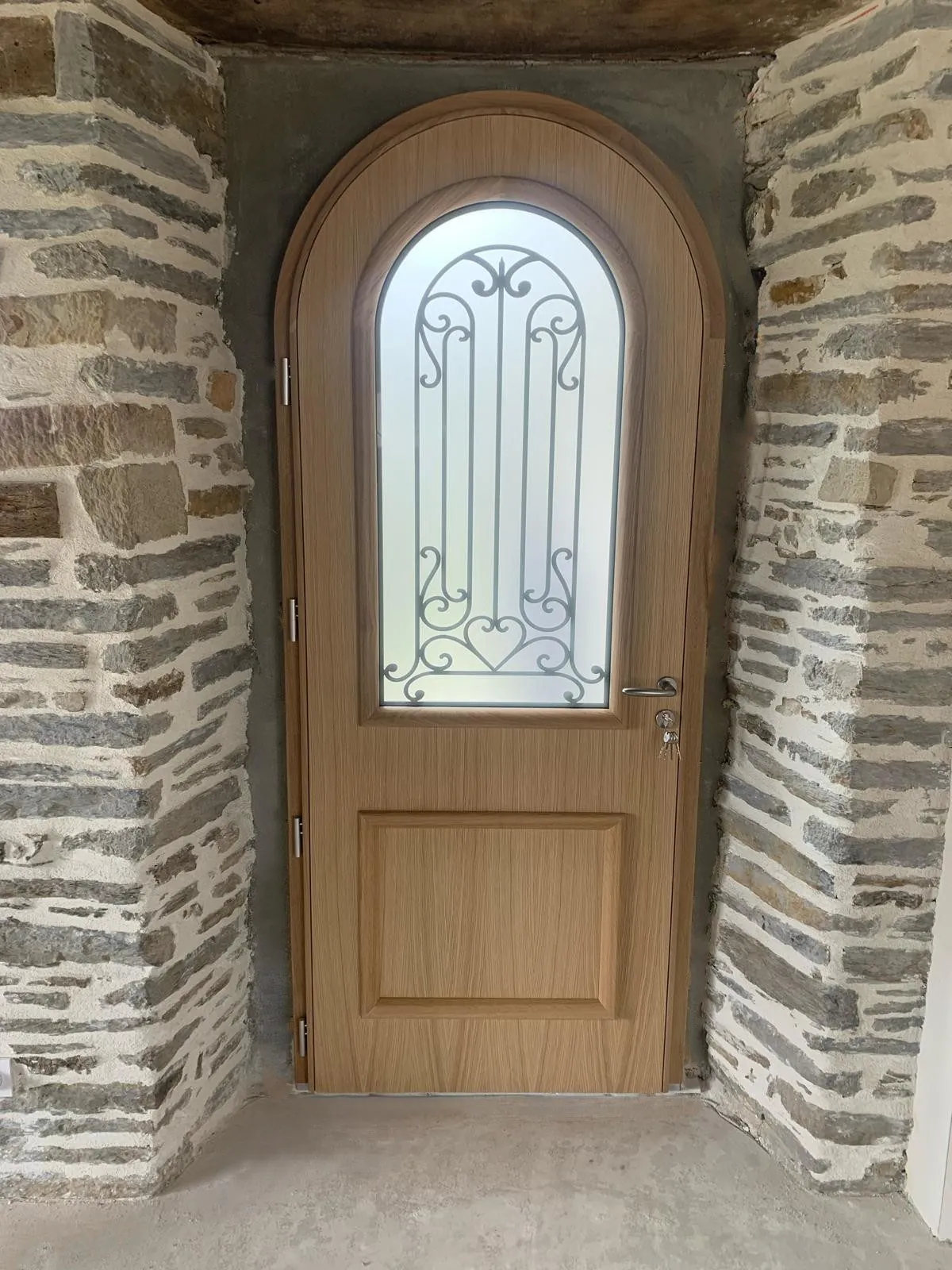 Porte d'entrée cintrée en bois chêne avec vitrage décoré de ferronnerie, posée par Maison Aubin à Gosné