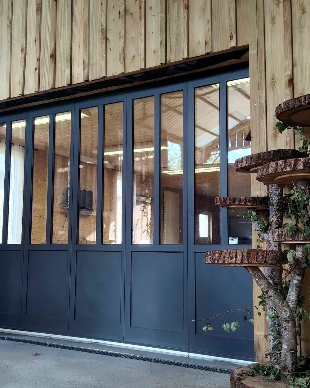Vue en perspective d'une porte de garage verrière GYPASS en aluminium sur bardage bois, posée par Maison Aubin, menuisier près de Vitré (35)